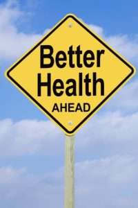 A yellow diamond shaped road sign with “Better Health AHEAD” in black block letters. Blue sky background with cumulus clouds. Overall a positive image.